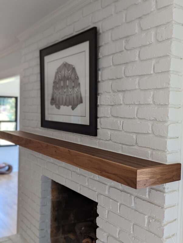 Wooden mantel on white brick fireplace.